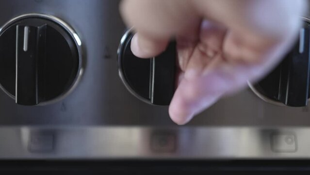 Closeup of a hand turning off the gas stove to save money due to the high price of natural gas in Europe.
