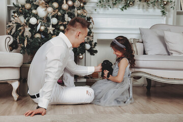 Happy father and daughter with cute griffin doggy at living room at cozy home of golden beautiful Christmas tree background fest. Family atmospheric moment Merry Christmas, Happy New Year, pet love