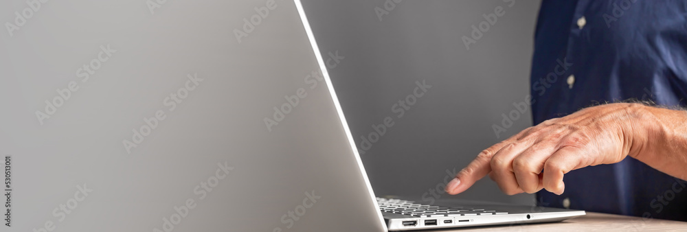 Poster Banner with mature man working on laptop. Forefinger at keyboard closeup. Male entering information. Using computer in work and study. Copy space