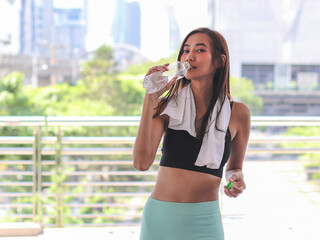 healthy and attractive Asian sportswoman in sportswear standing with  bridge fence and city building background, drinking water.