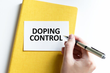 DOPING CONTROL text on a card on the background of a notebook on a table next to a person's hand...