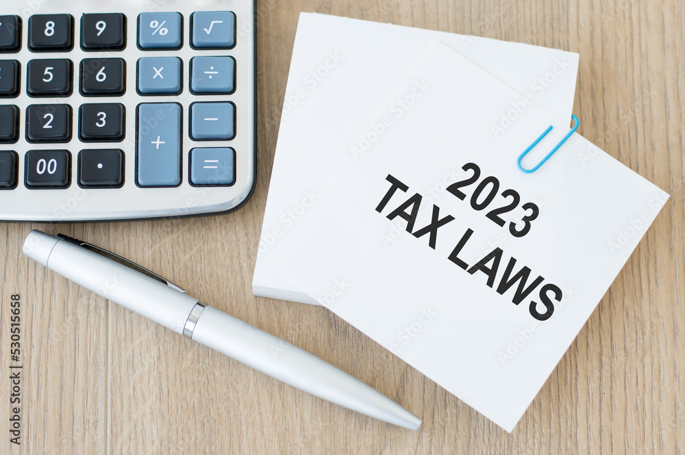 Poster taxe laws 2023 text on a card on a paper clip to a stack of cards for notes on a wooden table next t