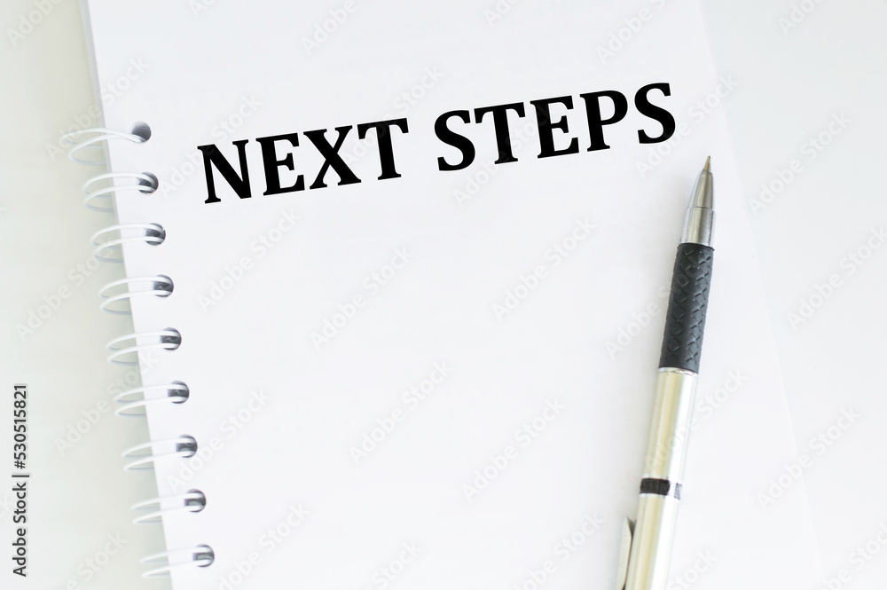 Poster next steps text on notepad on the table next to it is a pen