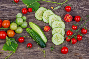 Sliced cucumbers and tomatoes on a branch on an old wooden background