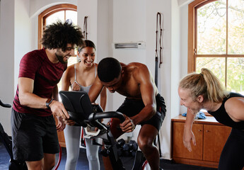 Group of multiracial young adults laughing with friend on exercise bike at the gym