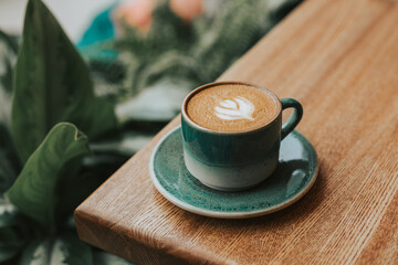 Delicious cappuccino with a beautiful foam in a green ceramic mug on a wooden table against a background of greenery. Atmospheric fresh coffee banner with space for text