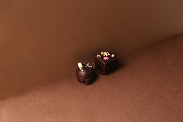 Two handmade chocolates on a brown background. Stylish and creative design of natural chocolate candies. Beautiful mocap of desserts