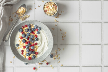 yogurt with blueberries, cranberries and granola on a light ceramic background, greek yogurt,...