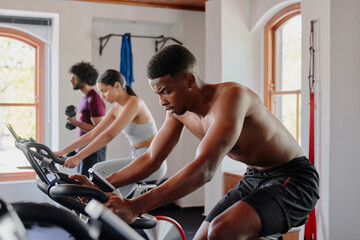 Group of young multiracial adults doing cardio on exercise bike at the gym