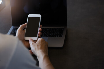 ノートパソコンの前でスマートフォンを操作する男性