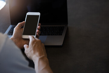 ノートパソコンの前でスマートフォンを操作する男性