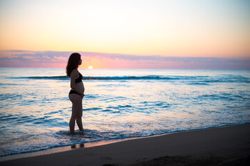 Preciosa fotografía de una mujer embarazada durante el amanecer en la playa. 