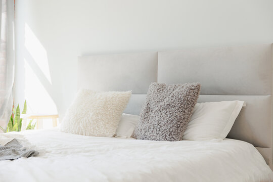 White bedroom scandinavian interior design with morning light on window. Warm fur pillows on grey bed