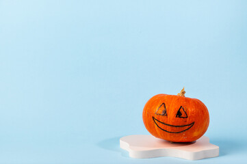 Small orange carved pumpkin on blue background with copy space. Concept celebration of Halloween or Thanksgiving. Cosmetics podium for halloween. Autumn still life.