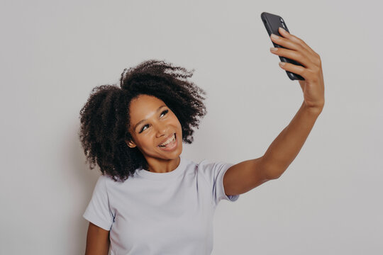 Cheerful young african woman with curly hair taking selfie on her modern mobile phone