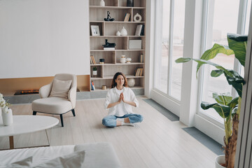 Female meditates practicing yoga sitting on floor, breathing fresh air in modern living room at home