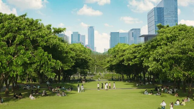People relax on the green lawn in public green park with cityscape background