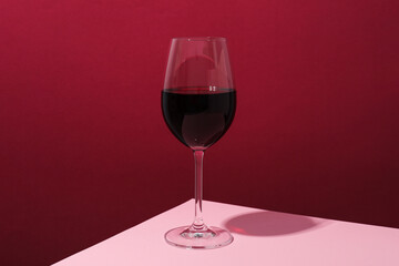 Glass of wine on pink table against crimson background