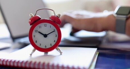 Red alarm clock and hands typing on computer keyboard
