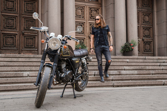 Portrait of cool guy with sunglasses and long hairs going to his custom bike.