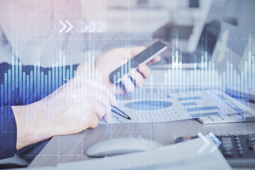 Double exposure of man's hands holding and using a digital device and forex graph drawing. Financial market concept.