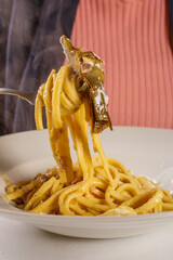 Piatto di pasta con carciofi, salsiccia e formaggio fuso servito in un ristorante napoletano