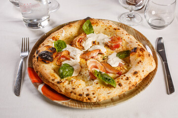 Pizza napoletana con mozzarella, pancetta, mozzarella, tarallo napoletano e basilico fresco servita in una pizzeria
