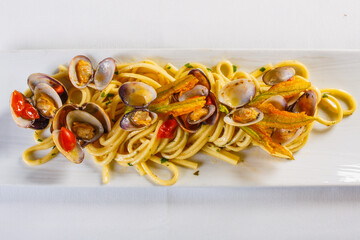 Piatto di spaghetti alle vongole, pomodorini e fiori di zucca servito in un ristorante elegante - obrazy, fototapety, plakaty