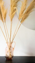 Vertical of dried pampas in a vase against a mirror and a white wall.