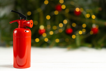 The fire extinguisher stands on a white table, against the background of a Christmas tree decorated...