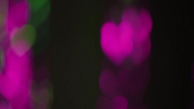 Bokeh glow. Romantic overlay. Love symbol. Blur gleam. Defocused neon pink green color hearts light motion on dark black abstract background.