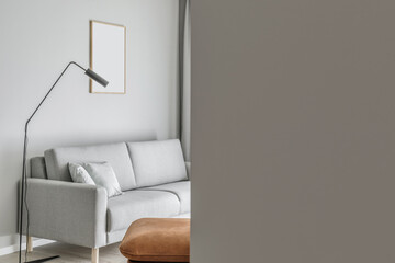 Modern minimalistic living room interior with grey sofa, leather seat, black elegant lamp. Aesthetic simple interior design concept.