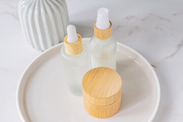 Skincare products set. Natural moisturizer cream jar, dropper bottle with serum and essence on round ceramic tray on marble background. Organic cosmetics concept