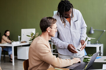 Obraz premium African businessman talking about windmill with his colleague while he working on laptop at office