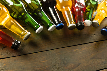 Image of various coloured glass beer bottles with crown caps, with copy space lying on wood - obrazy, fototapety, plakaty