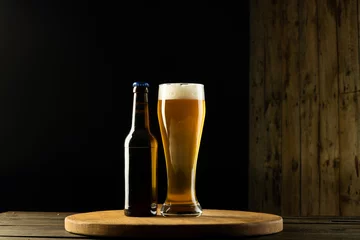 Foto op Canvas Image of full bottle and pint glass of beer on wooden table, with copy space © vectorfusionart