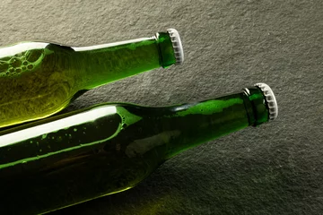 Foto op Canvas Image of two green glass beer bottles with white crown caps lying on slate, with copy space © vectorfusionart