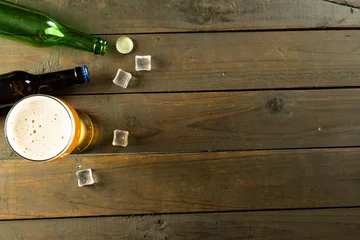 Foto op Canvas Image of two glass beer bottles, pint of beer and ice cubes lying on wooden table, with copy space © vectorfusionart
