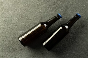 Foto op Canvas Image of two dark beer bottles with blue crown caps lying on slate, with copy space © vectorfusionart