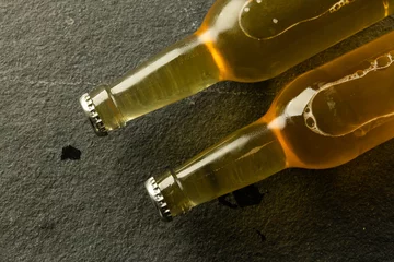 Foto op Canvas Image of two clear glass beer bottles with crown caps lying on slate, with copy space © vectorfusionart