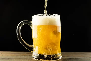 Foto op Canvas Image of beer pouring into glass tankard of foamy beer on wooden table, with copy space © vectorfusionart