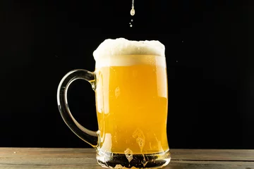 Foto op Canvas Image of beer pouring into glass tankard of foamy beer on wooden table, with copy space © vectorfusionart