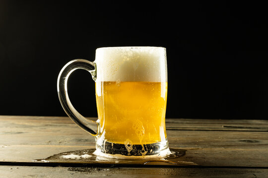 Image of glass tankard full of foamy beer on wooden table, with copy space