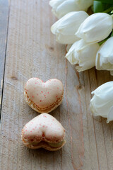 8 march. Two creamy macarons are lying on the wooden table with white tulips. Two macarons in form of the heart as 8. Dessert is on the wood
