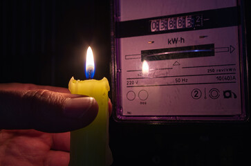 Burning candle near a domestic electric meter in darkness. Power outage, blackout, load shedding,...