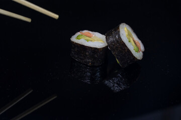 two pieces of sushi with chopsticks in dark background