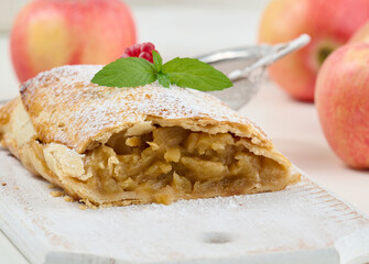 Baked strudel with apples sprinkled with powdered sugar on a white wooden board, delicious dessert