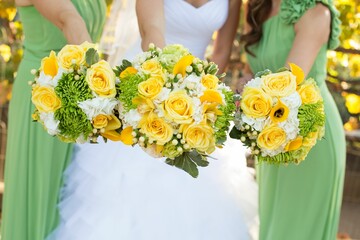 Closeup of a bride and bridesmaids holding beautiful yellow rose bouquets during a wedding ceremony