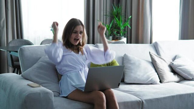 Overjoyed happy female looking at laptop screen feeling joy and euphoria, raising hands, feeling happy. Young woman getting great news about promotion