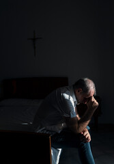 Portrait of adult man sitting on bed against window with sunlight and shadow